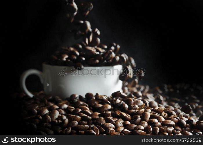 Cup filled with hot fresh steaming coffee beans on black