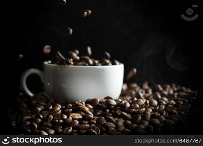Cup filled with hot fresh steaming coffee beans on black