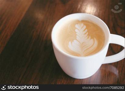 Cup of art latte or cappuccino coffee on wooden table with copy space in the cafe