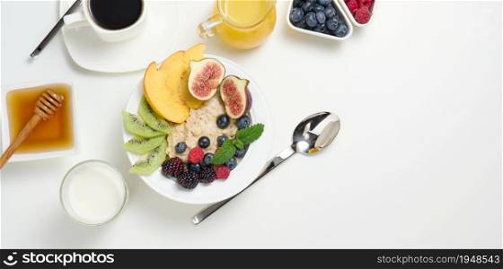 cup of black coffee, a plate of oatmeal and fruit, honey and a glass of milk on a white table, a healthy morning breakfast, top view, copy space