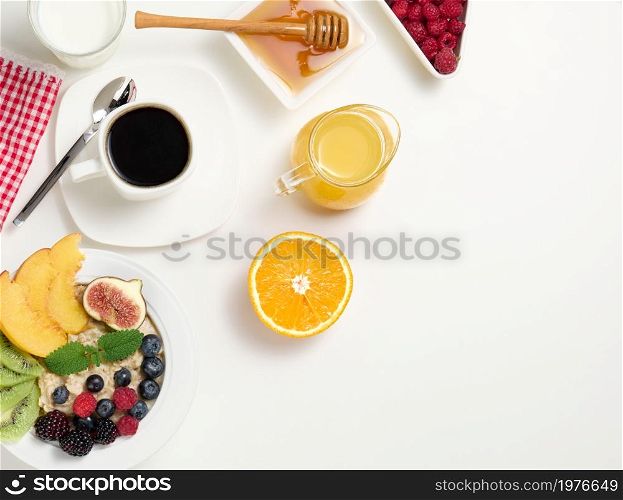 cup of black coffee, a plate of oatmeal and fruit, honey and a glass of milk on a white table, a healthy morning breakfast