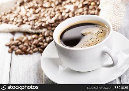 cup of black coffee and beans on wooden table