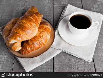 Cup of black coffee and croissant for breakfast on wooden background