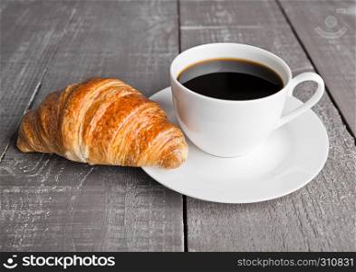 Cup of black coffee and croissant for breakfast on wooden background