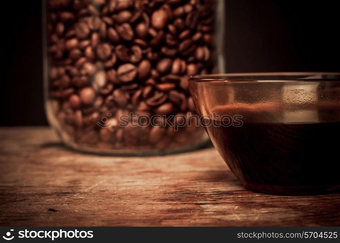 Cup of black coffee and jar of beans on a wooden table