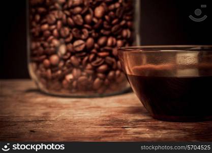 Cup of black coffee and jar of beans on a wooden table