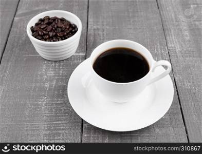 Cup of black coffee for breakfast with beans on wooden background