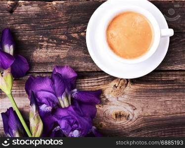 cup of black coffee with a bouquet of blue irises on a gray wooden background, top view