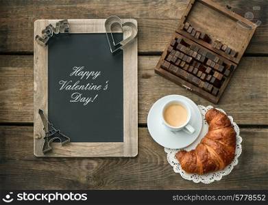 Cup of black coffee with croissant, blackboard and heart decoration on rustic wooden background. romantic Valentine&rsquo;s Day breakfast