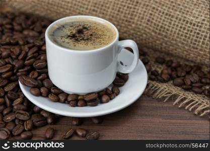 Cup of black coffee with roasted coffee beans on the dark wooden background with rough burlap. Cup of coffee and coffee beans