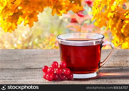 Cup of black tea, viburnum berries on a rustick wooden table. Black tea in a transparent cup with a blurry background.