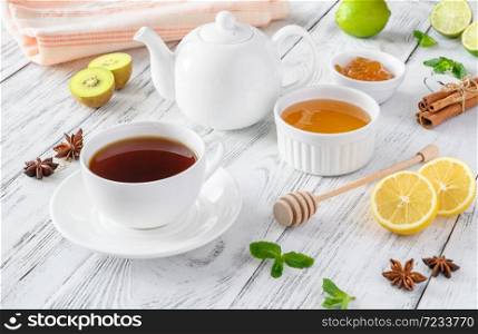 Cup of black tea with fresh fruits, honey, jam and spices on wooden background