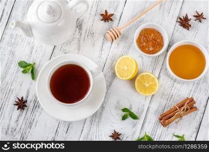 Cup of black tea with honey, jam and spices on wooden background: top view