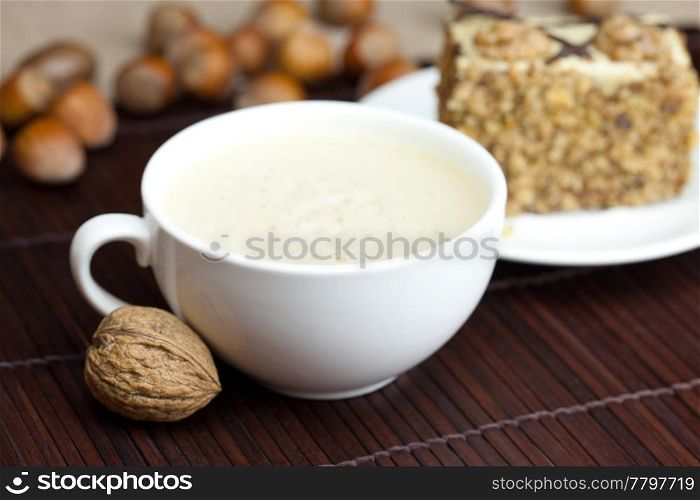 cup of cappuccino, a piece of cake with nuts on a plate lying on a bamboo mat
