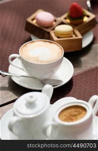 Cup of cappuccino and macaroons in outdoor cafe, selective focus