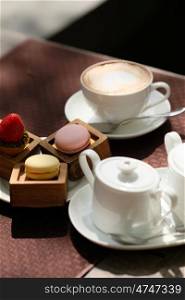 Cup of cappuccino and macaroons in outdoor cafe, selective focus
