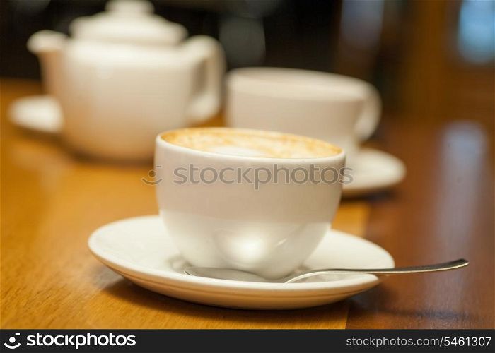 Cup of cappuccino and teapot on background