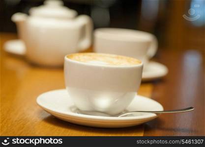 Cup of cappuccino and teapot on background
