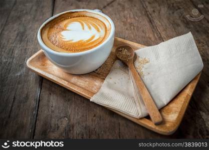 Cup of cappuccino coffee on wooden plate and brown sugar in spoon. Food background in vintage style