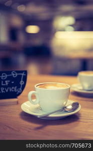 Cup of cappuccino, plate with self-service text on it