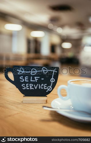 Cup of cappuccino, plate with self-service text on it