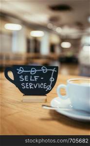 Cup of cappuccino, plate with self-service text on it