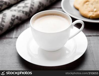 Cup of cappuccino with grey wool scarf and cookies on wooden background