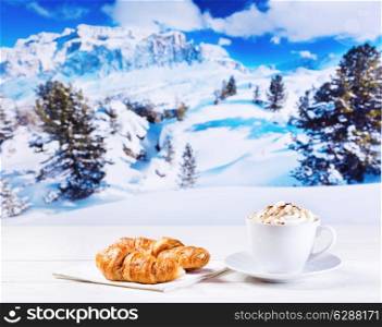 cup of cappuccino with whipped cream and croissants on wooden table over winter landscape