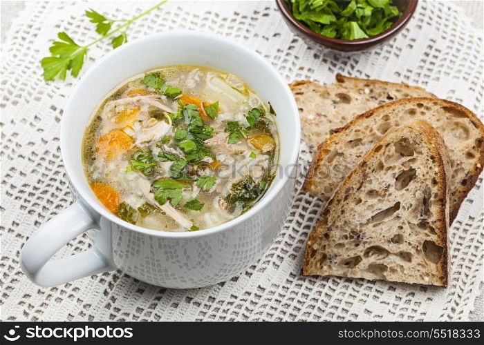 Cup of chicken rice soup. Cup of hot chicken rice soup served with bread and parsley on crochet tablecloth