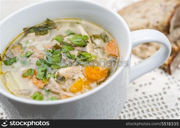 Cup of chicken rise soup. Cup of hot chicken rice soup served with bread on crochet tablecloth closeup