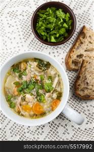Cup of chicken soup. Cup of hot chicken rice soup served with bread and parsley from above on crochet tablecloth