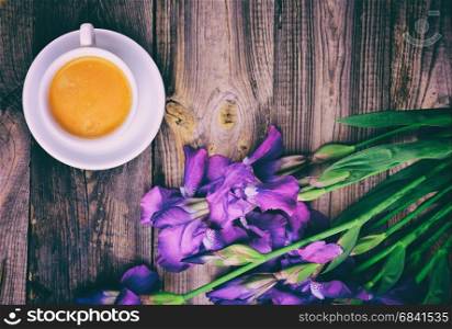 Cup of coffee and a bouquet of blue irises on a gray wooden background, top view, vintage toning