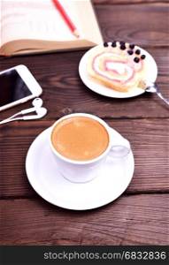 cup of coffee and a mobile phone on a brown table, close up