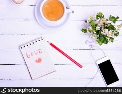 cup of coffee and a smartphone with headphones on a white wooden background, top view