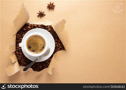 Cup of coffee and beans in torn paper. Coffee ingredients with espresso at table