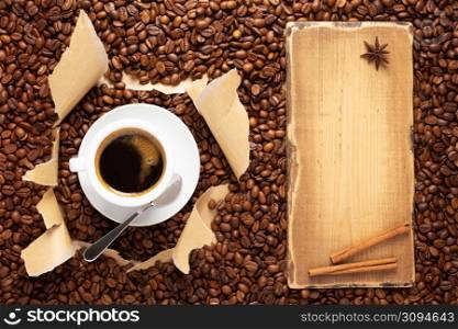 Cup of coffee and beans in torn paper. Coffee ingredients with espresso at table