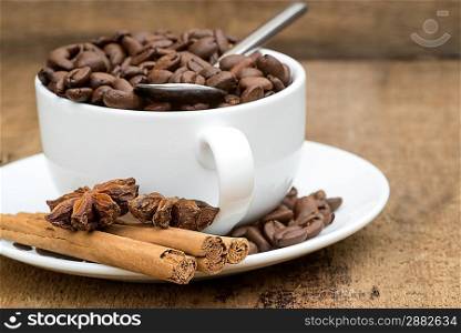 Cup of coffee and beans with cinnamon sticks and star anise on wooden background