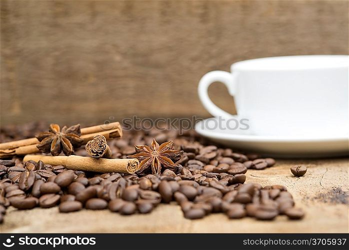Cup of coffee and beans with cinnamon sticks and star anise on wooden background