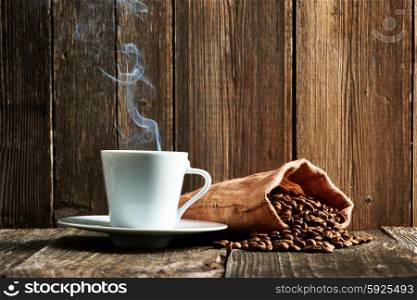 Cup of coffee and coffee beans in bag on wooden table