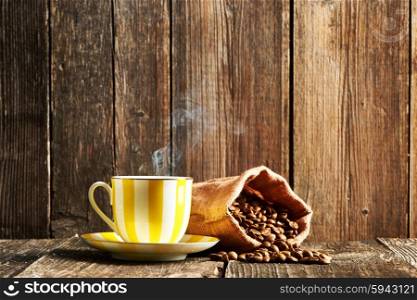 Cup of coffee and coffee beans in bag on wooden table