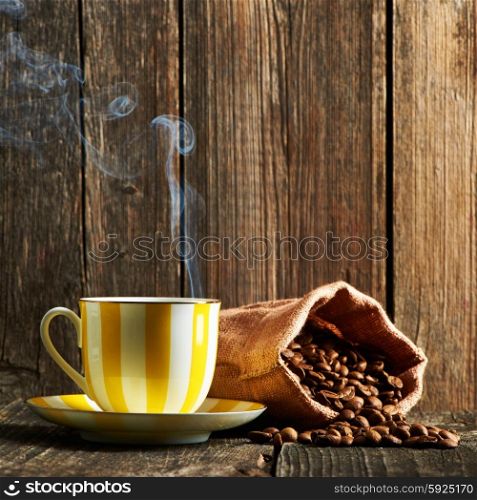 Cup of coffee and coffee beans in sack on wooden table