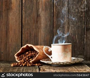 Cup of coffee and coffee beans in sack on wooden table