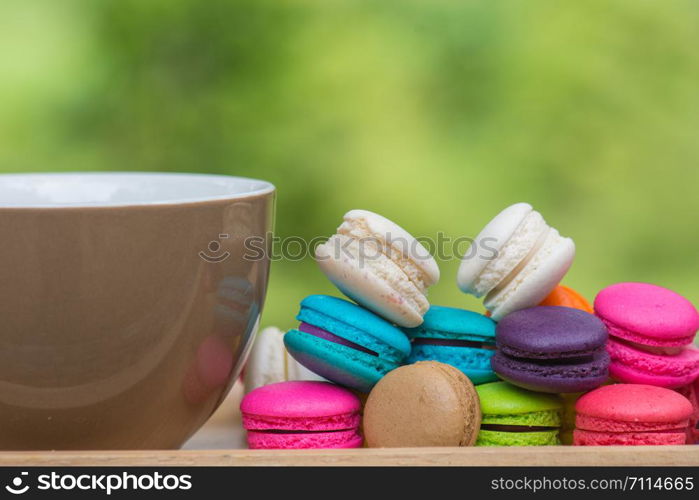 Cup of coffee and Colorful Macaroons in dish on wooden table in garden