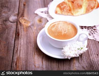 Cup of coffee and croissant on gray wooden background, top view