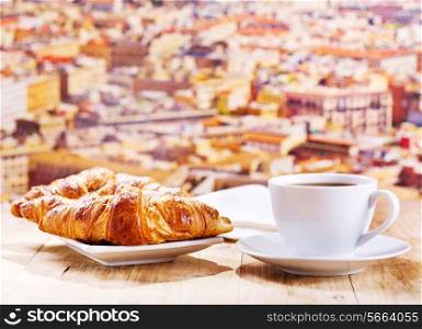 cup of coffee and croissants on wooden table over cityscape