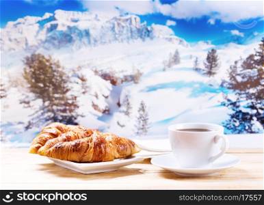 cup of coffee and croissants on wooden table over winter landscape