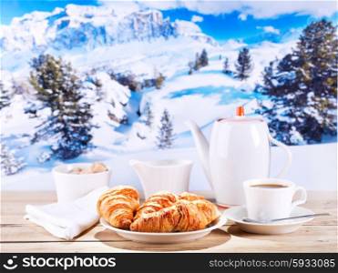 cup of coffee and croissants on wooden table over winter landscape