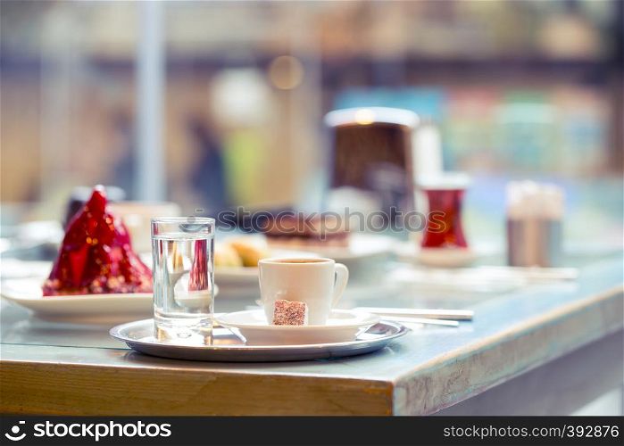 Cup of coffee and glass of clean water on tray in cafe. White cup with coffee and glass of water is standing on table in cafe against the background of cake and window. Selective focus. Cup of coffee and glass of clean water on tray