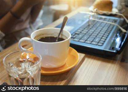 Cup of coffee and laptop on wooden table in coffee shop