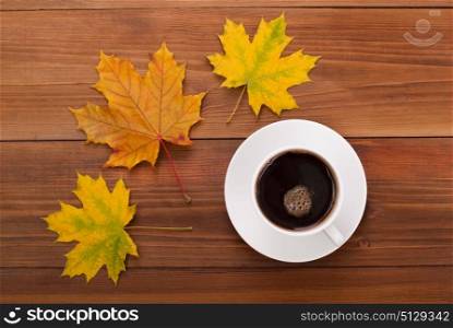 Cup of coffee and maple leaves on a wooden table.